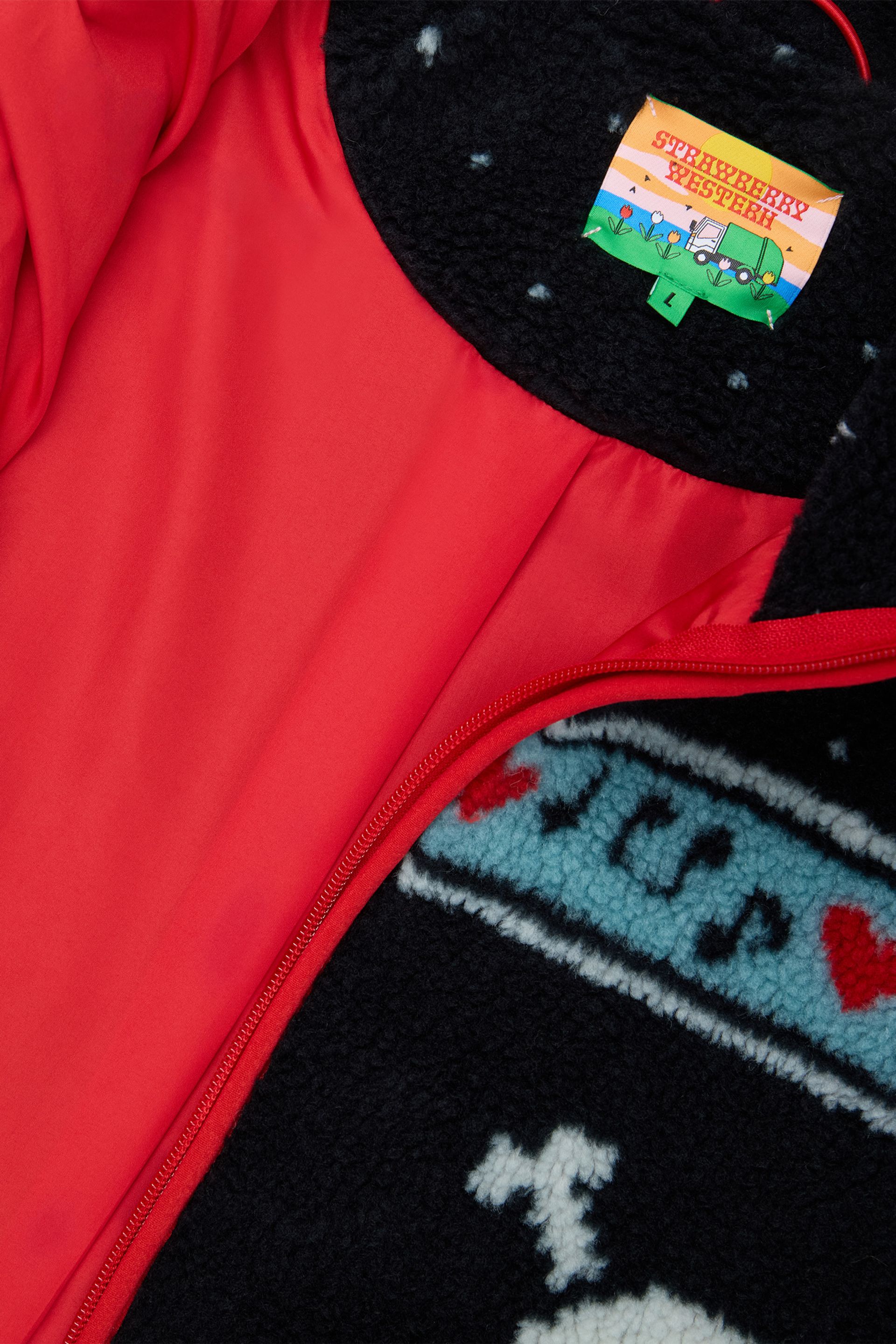 Detailed view of a black multi sherpa jacket featuring white skull and crossbones patterns, red hearts, and light blue musical note designs across the chest and sleeves