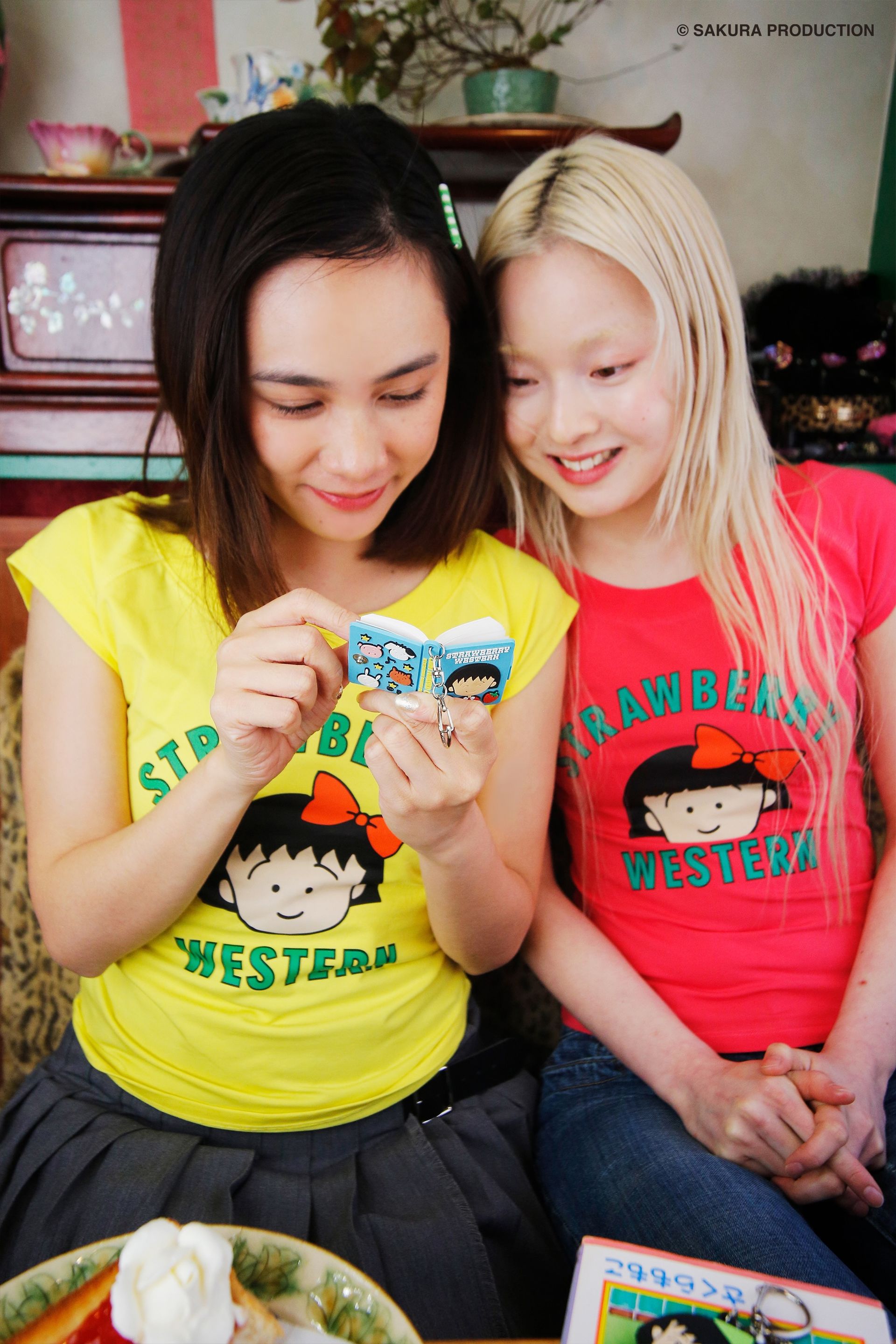 Two girls sitting together smiling as the girl on the left writes on the Chibi Maruko Chan Secret Notebook.