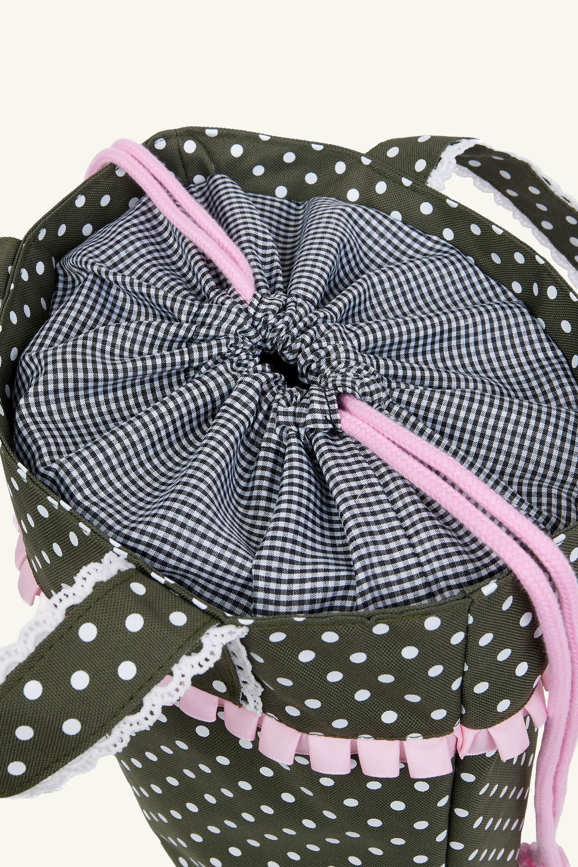 Detail view of the black and white gingham lining cinch closure on the olive green polka dot ruffle trim shoulder bag.