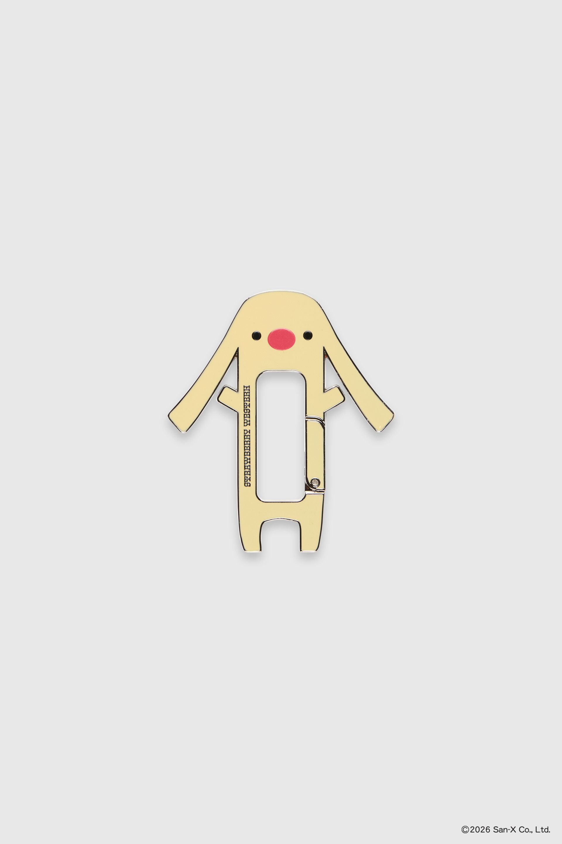 Flat image of Toto carabiner, shaped like a dog/bunny hybrid with long, floppy ears and a big red nose. The skin color is yellow with two black dots for eyes. Strawberry Western logo on the front.