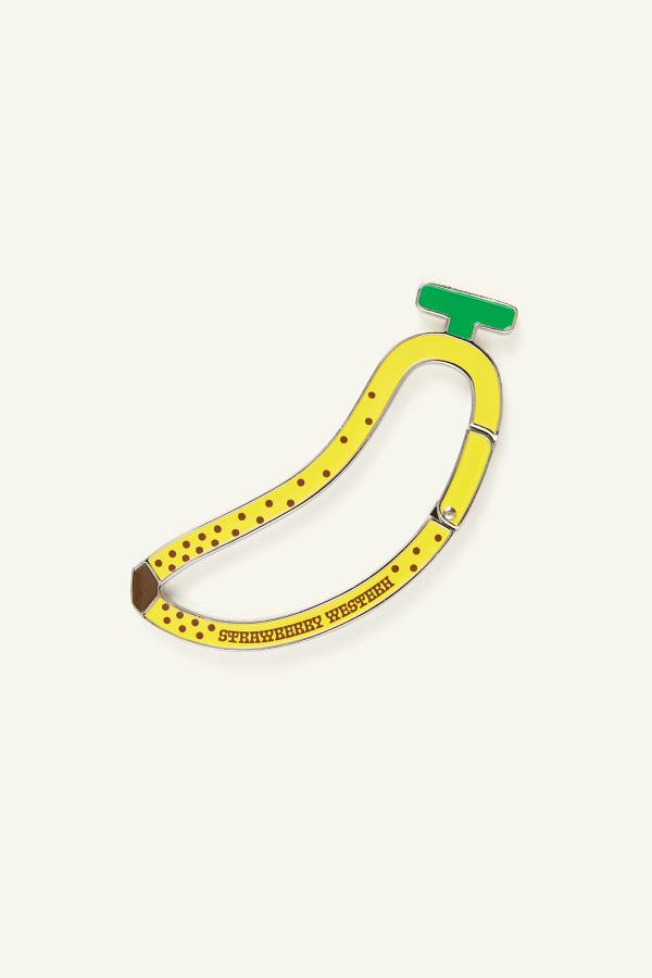 Kawaii banana shaped metal carabiner keychain clip made from zinc alloy with yellow and green enamel fill and printed brown polka dots and Strawberry Western logo on both sides.