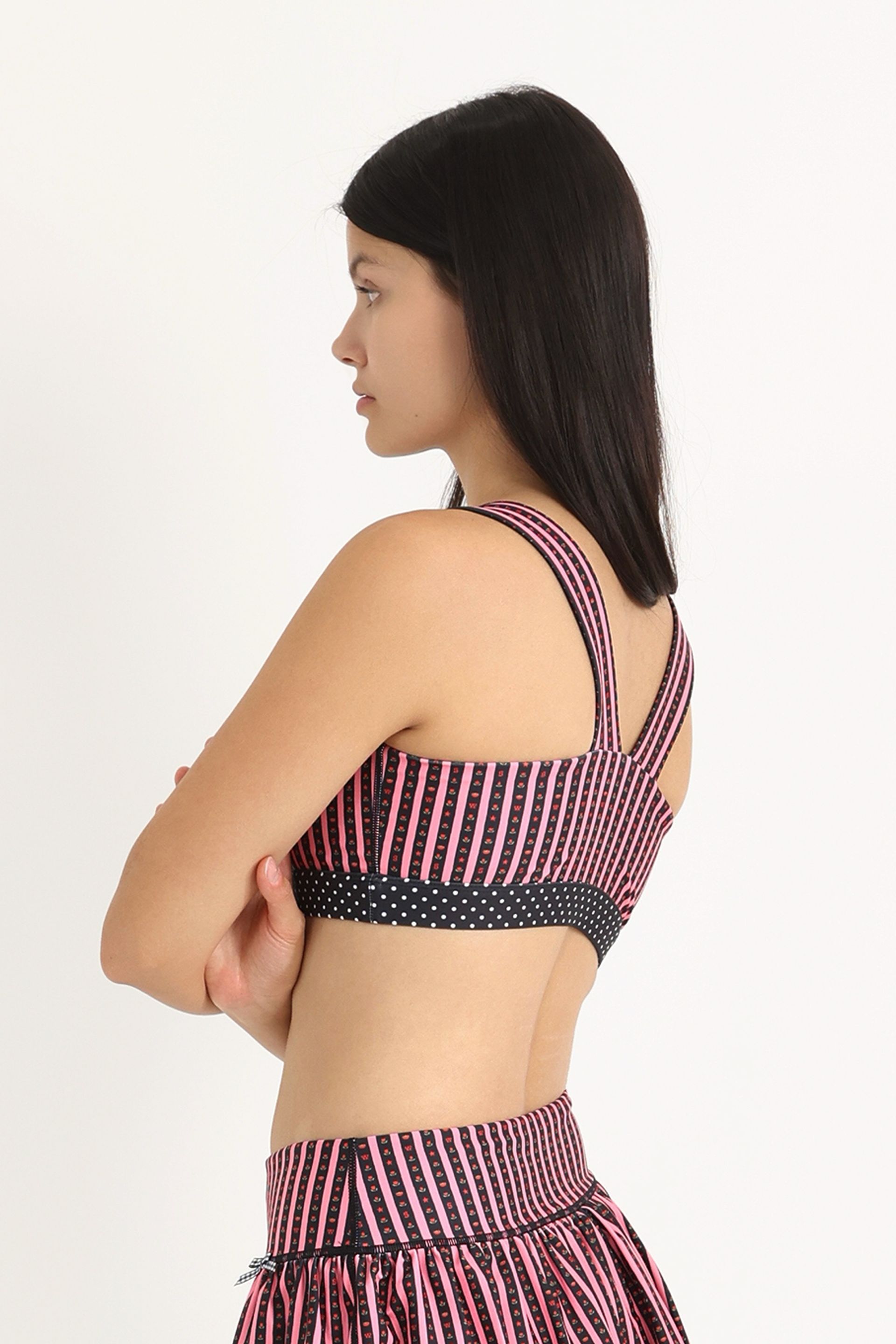 Back view of medium-support Coco Sports Bra silhouette featuring a hand-drawn, floral border stripe print  in Pink/Black with contrast polka dot print elastic band and gingham bow details.