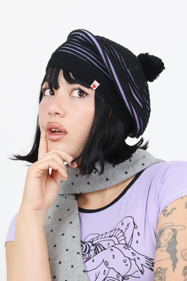 Model wearing lavender and black dimensional striped knit beret beanie with decorative pompom.