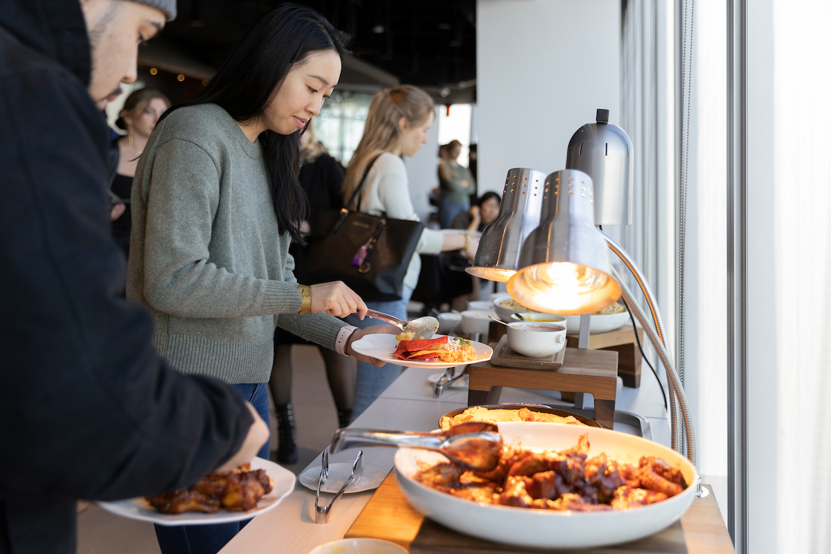 An asian woman holding a plate of food by a table with an assortment of other delicacies.