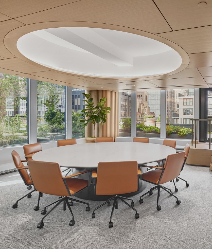 A spacious conference room with a round table surrounded by brown-leather chairs 