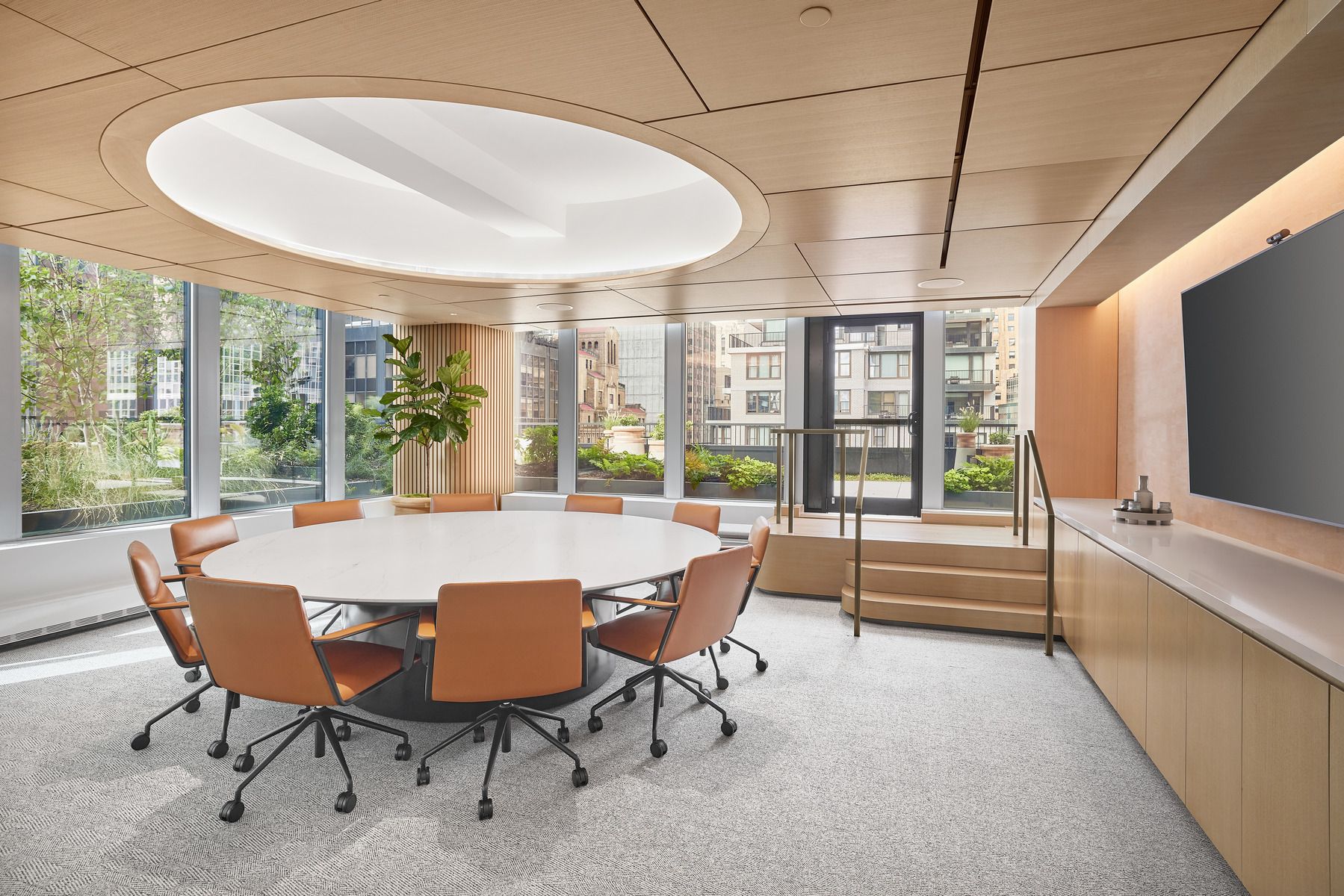A spacious conference room with a round table surrounded by brown-leather chairs 