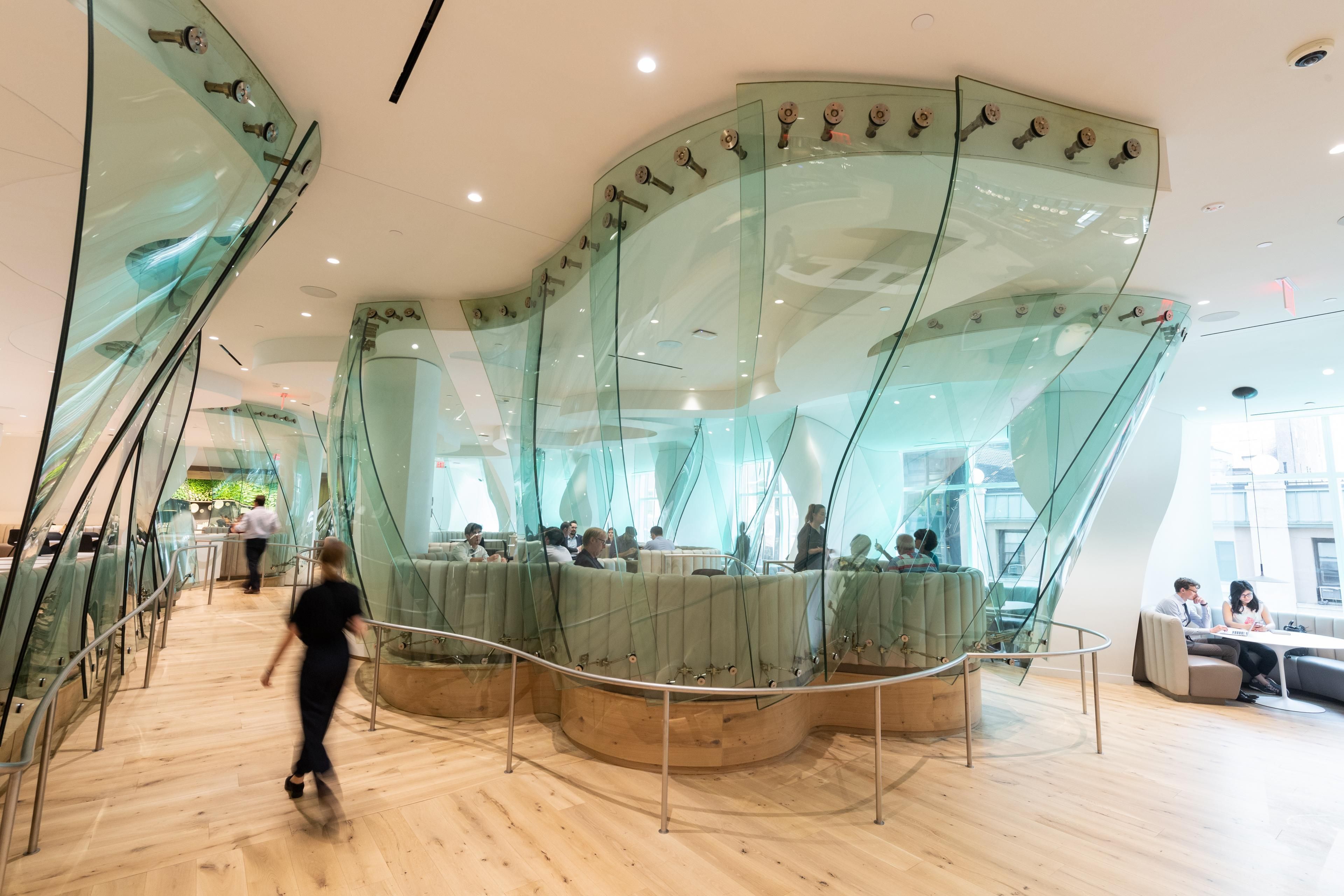 Well& by Durst at One Five One: A modern, airy cafe interior featuring curved glass partitions. A bright space with natural light. Staff supervising the area.