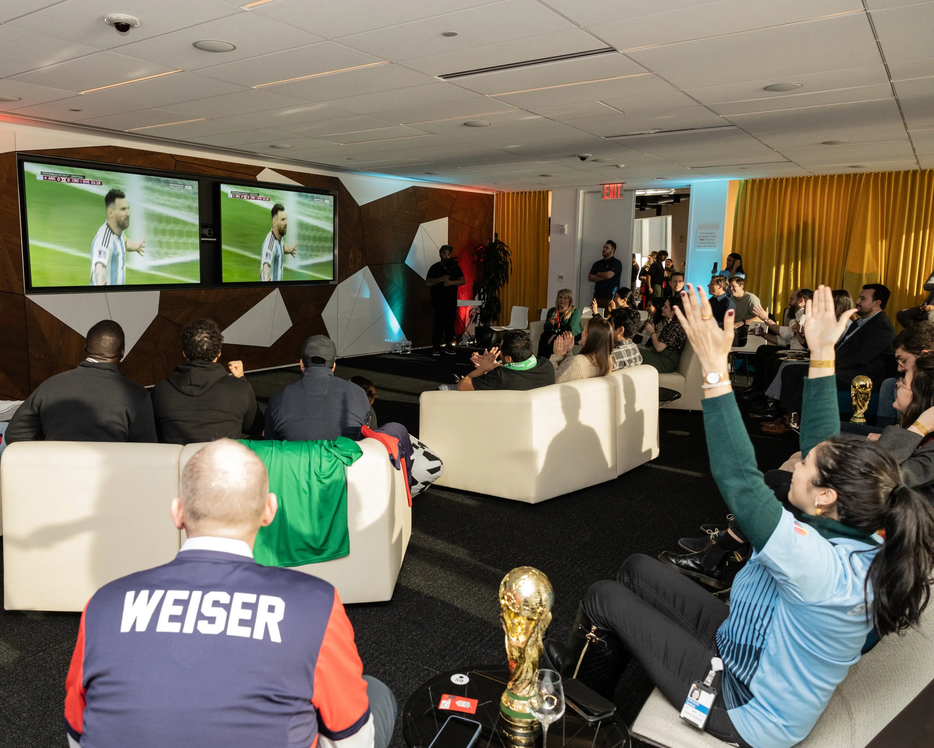 A diverse group of individuals sitting in Well& by Durst's conference space, focused on watching a soccer game on a large screen.