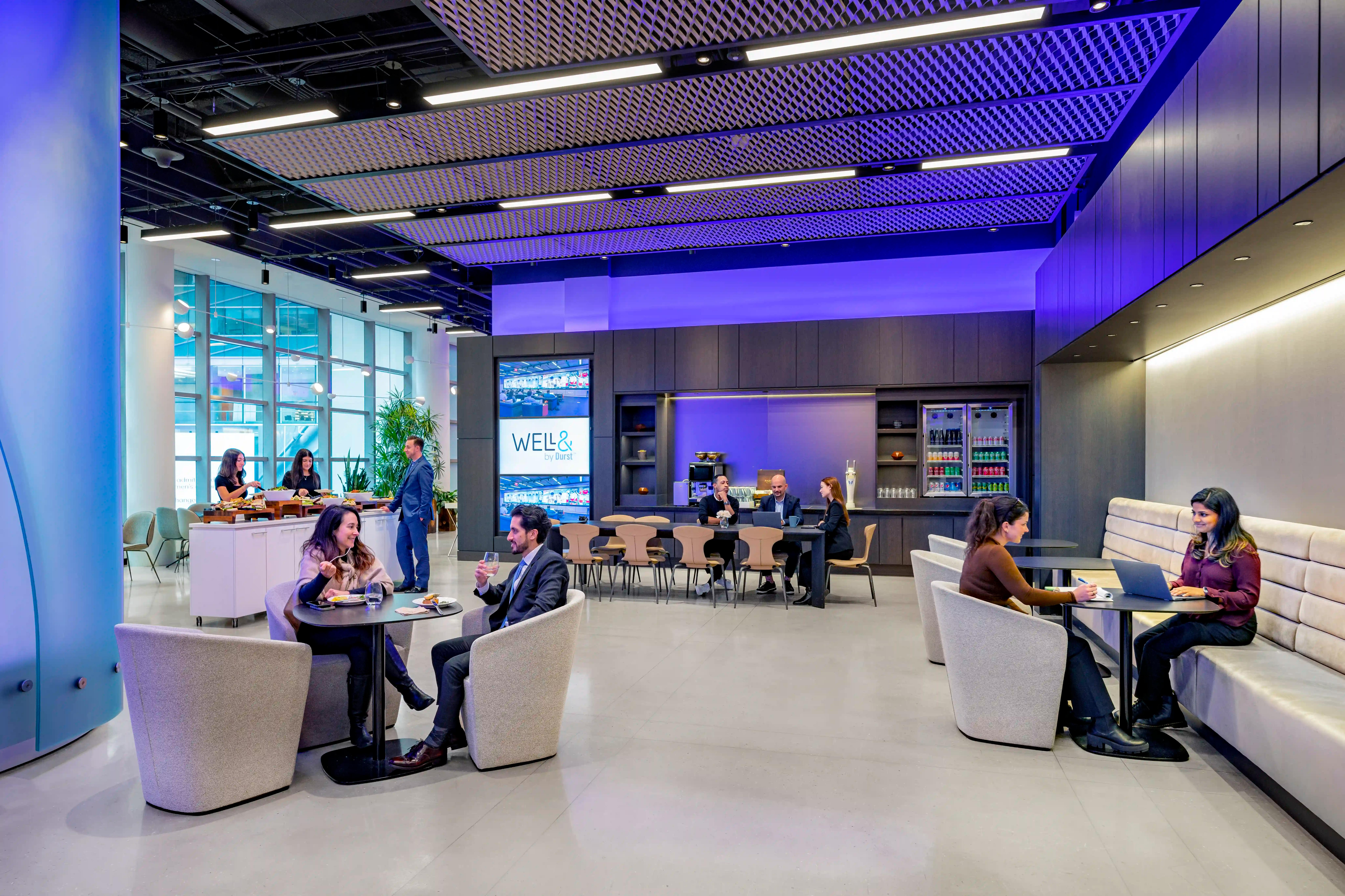 People gathered in a building's amenity space, Well& by Durst, sitting at tables and engaging in conversations at One Five One.