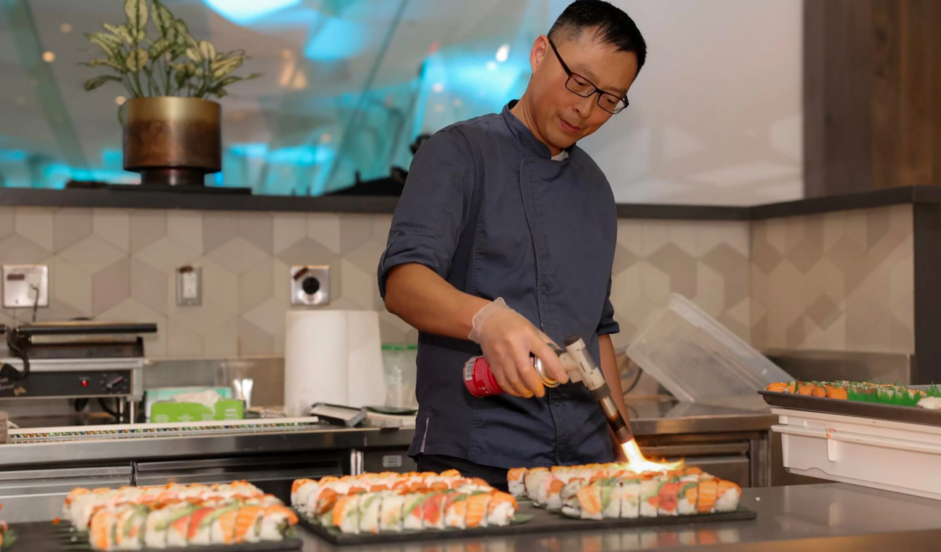 A man in a blue shirt skillfully prepares sushi in the kitchen.