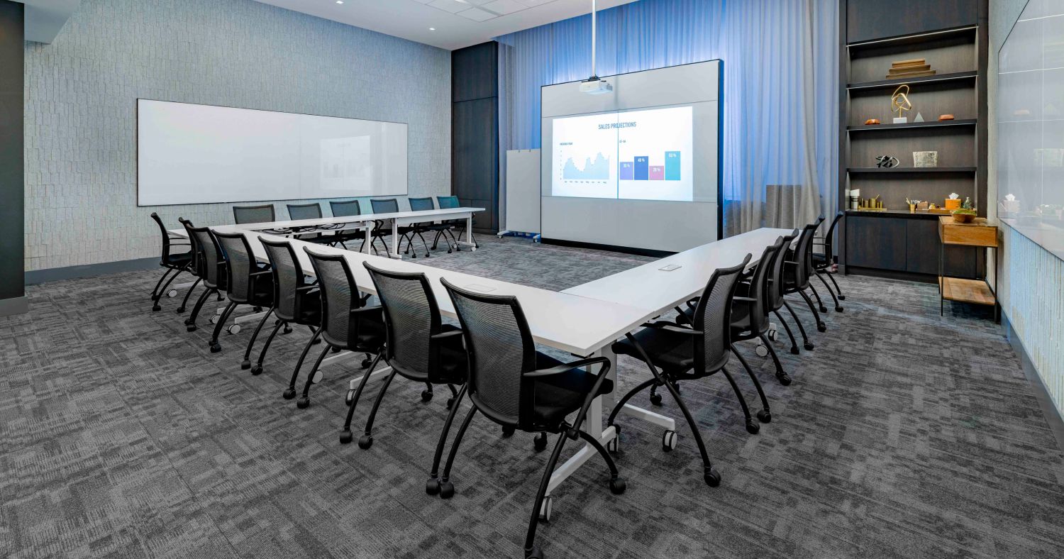 151 West 42nd meeting space filled with empty chairs arround desks and a large screen at end of a wall. 