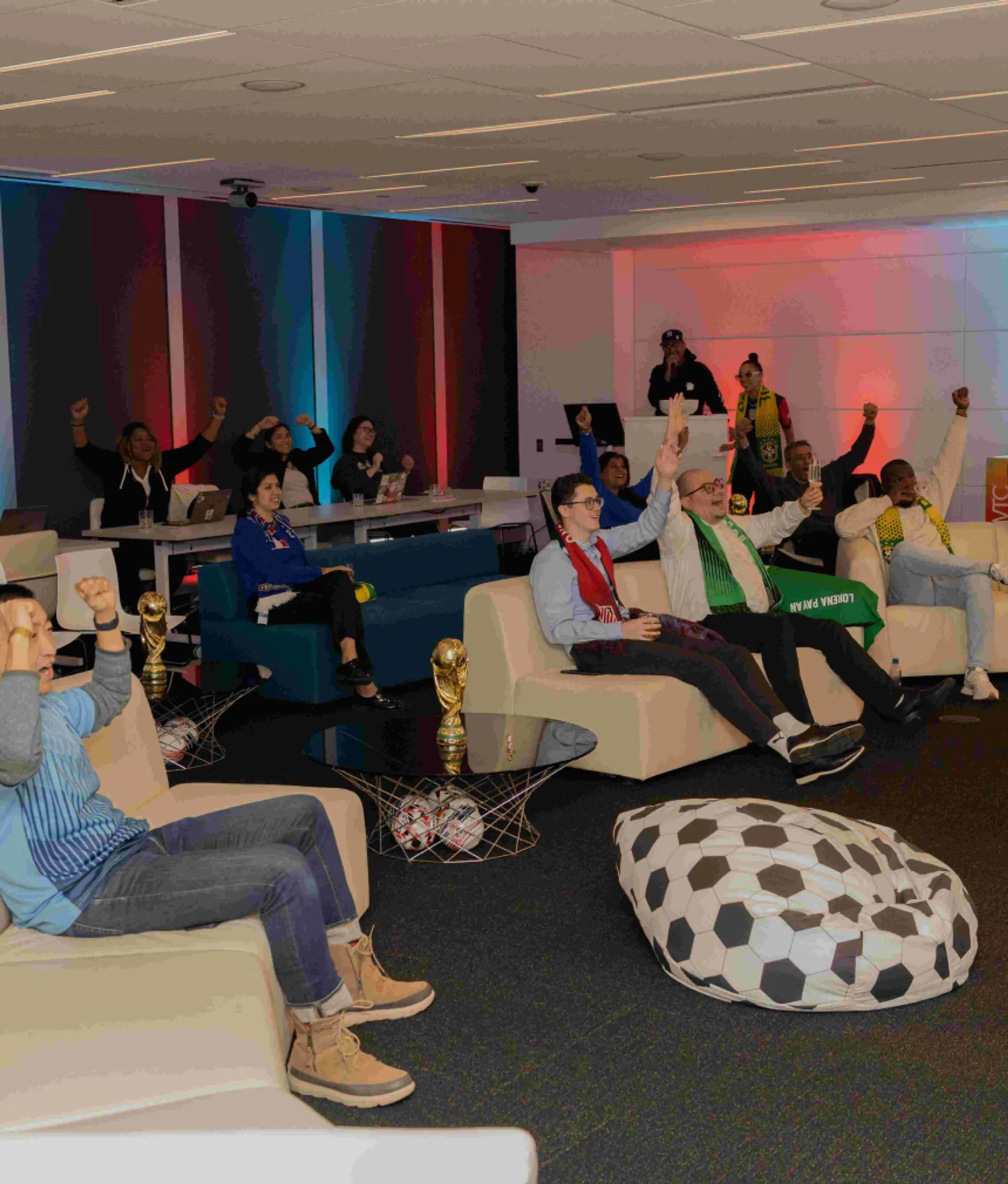A diverse group of professionals sitting in a decorative lounge at an event watching the World Cup on a screen.
