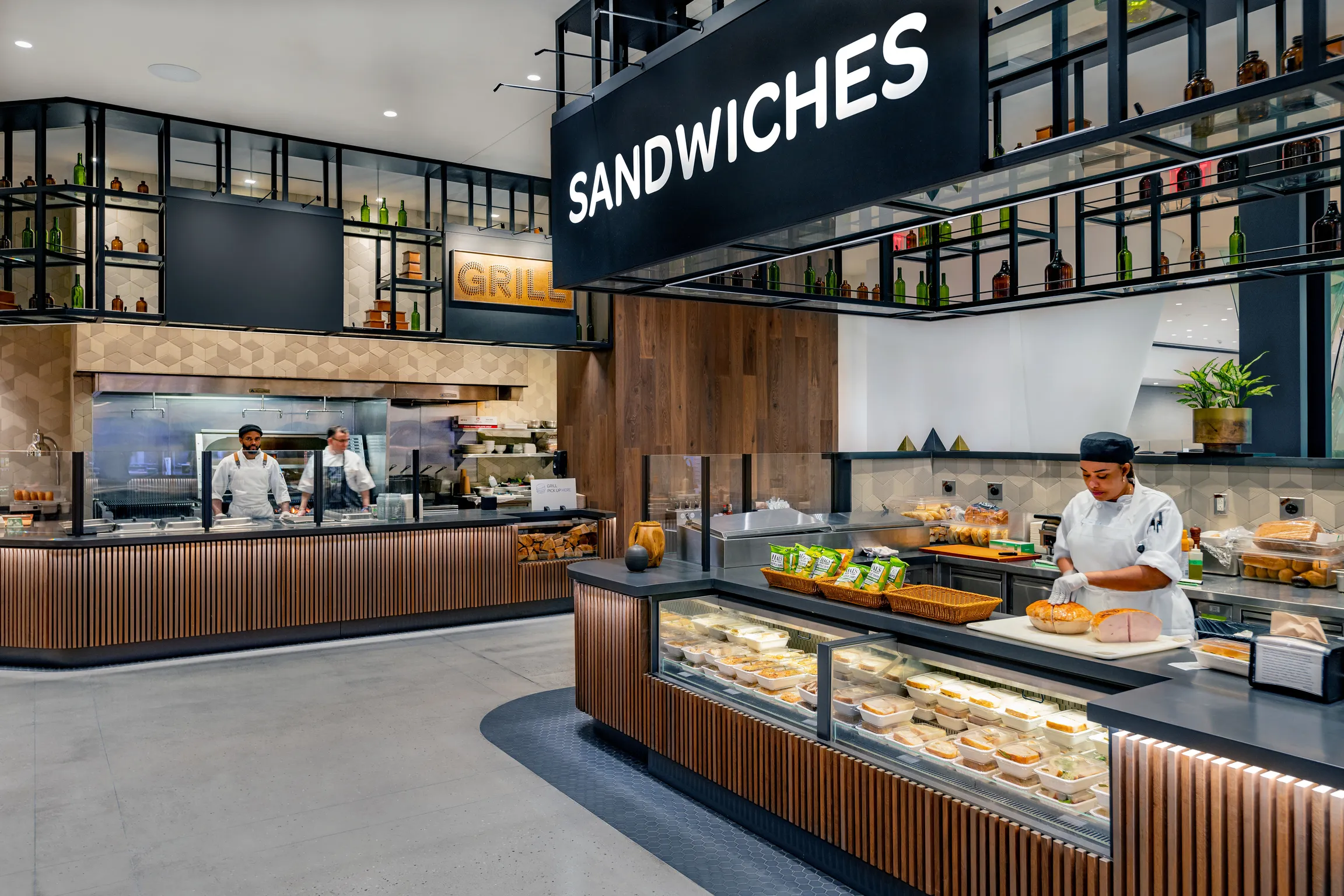 The Grill and Sandwich stations in the Food Hall at Well& by Durst with staff serving customers.