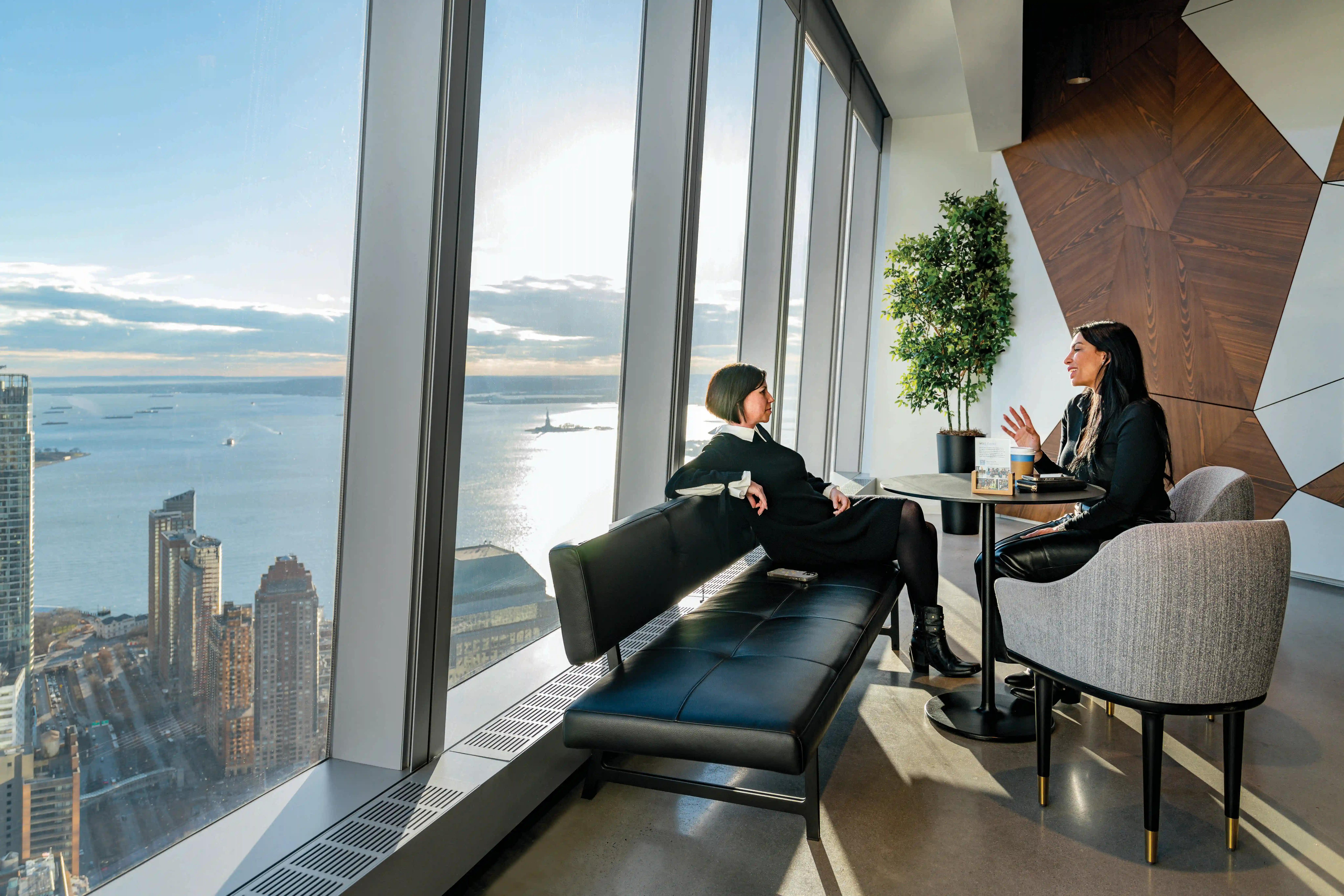 Two people sitting at a table near a large window, enjoying the city view outside.