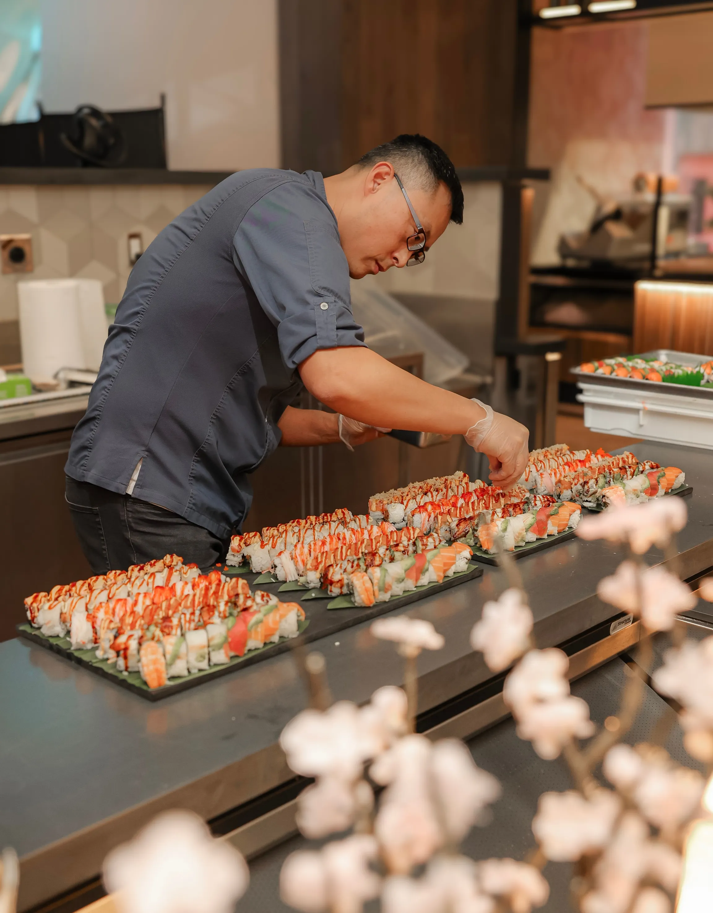 A skilled sushi chef in a blue shirt meticulously decorating sushi rolls