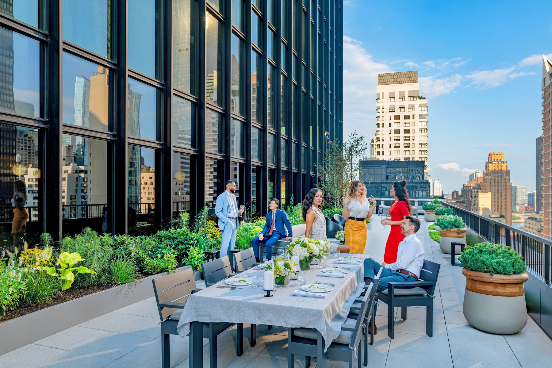 People sitting at a table on the 825 Third Avenue wrap-around terrace, enjoying a meal with a city skyline in the background