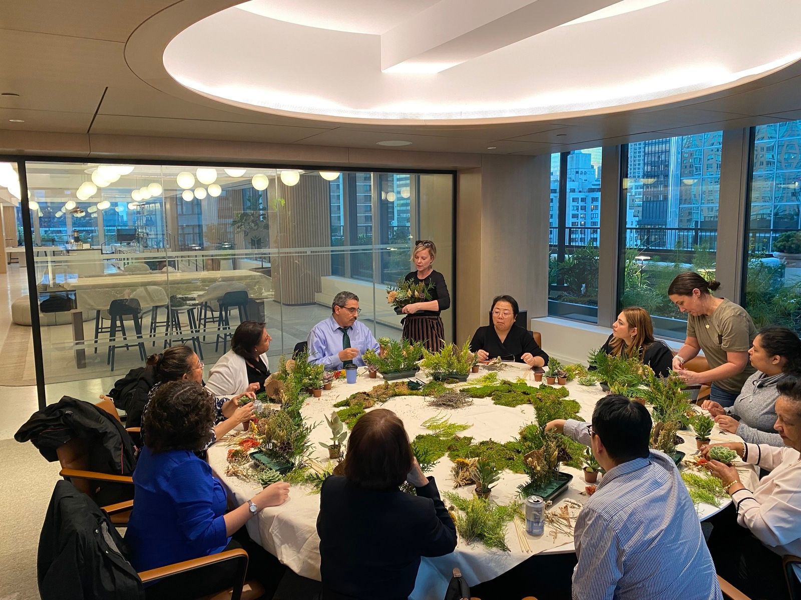 Individuals seated at a table with plants, taking part in a class focused on creating mini terrariums