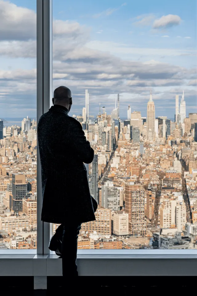 A man gazing out a window at a city skyline from the 64th floor sky lobby of One World Trade Center.