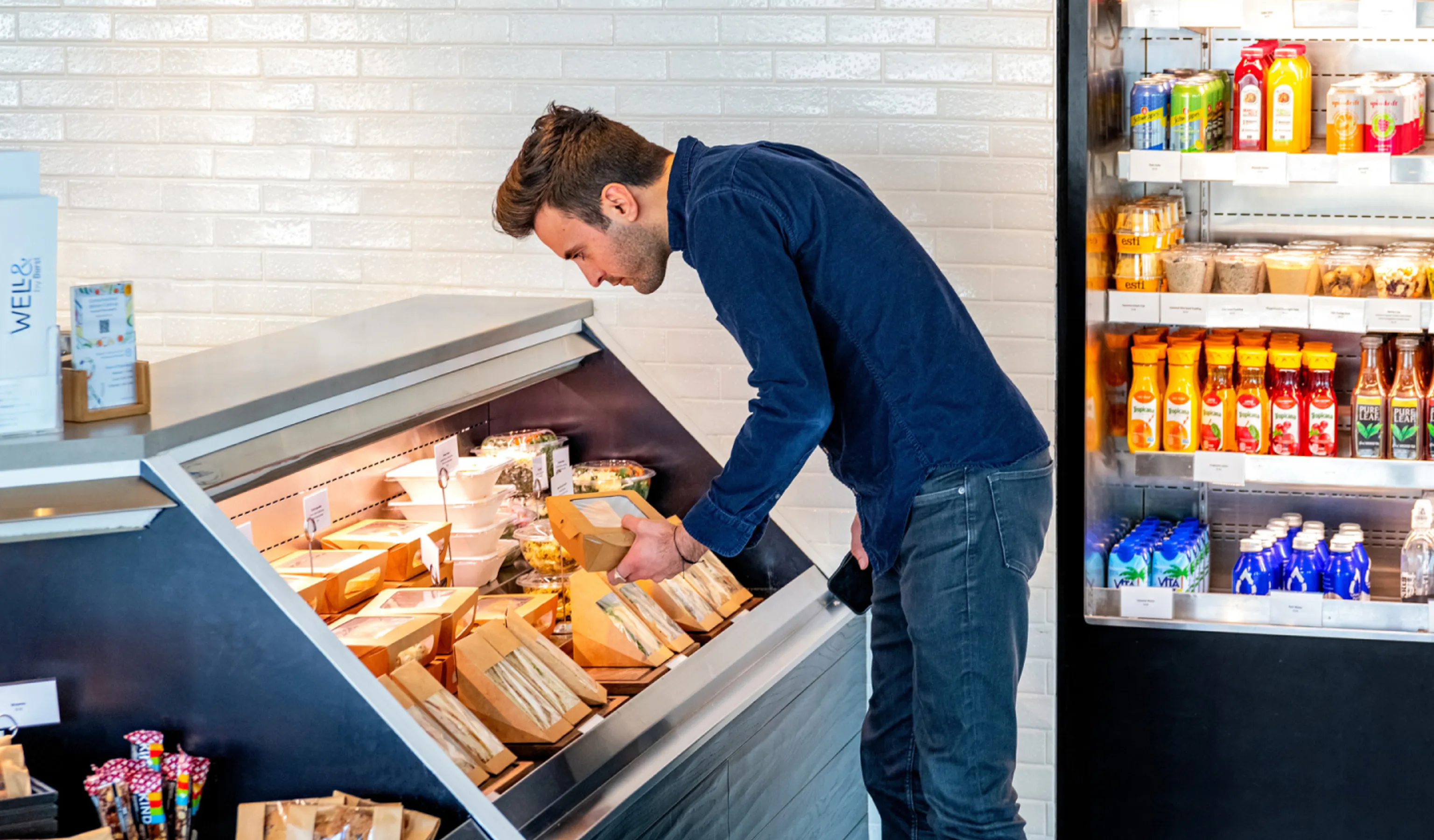 A man checking out different food options on display in Well& by Durst's cafe floor.