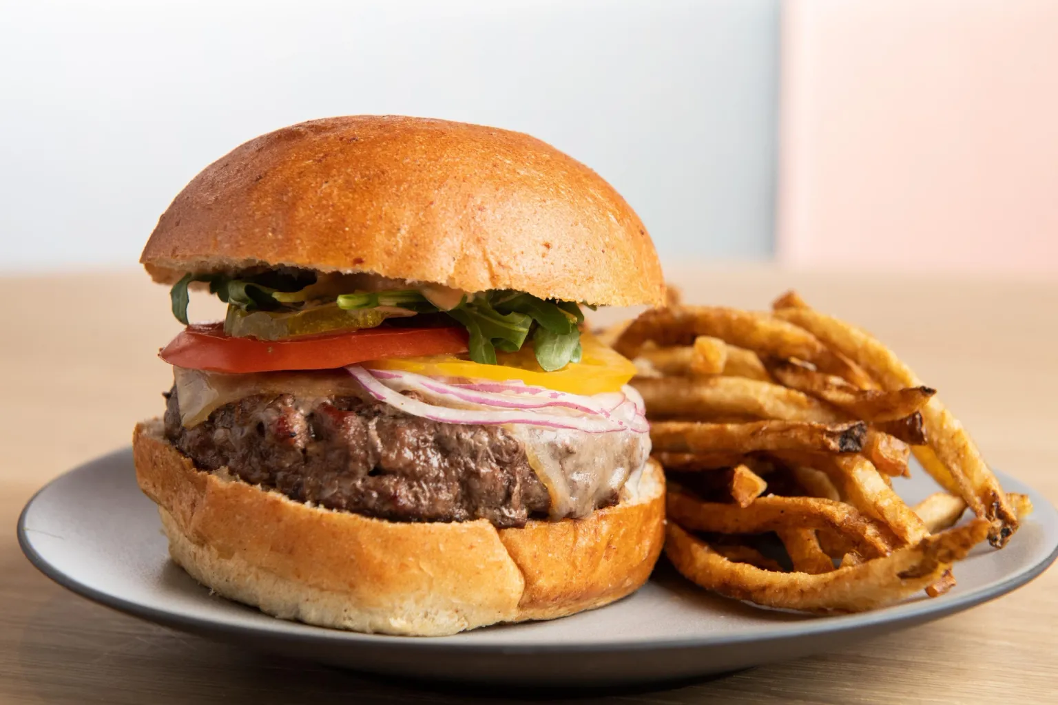 A juicy cheeseburger with a toasted bun, topped with lettuce, tomato, cheese, and a beef patty, sits on a white plate next to a generous serving of crispy, golden-brown French fries.