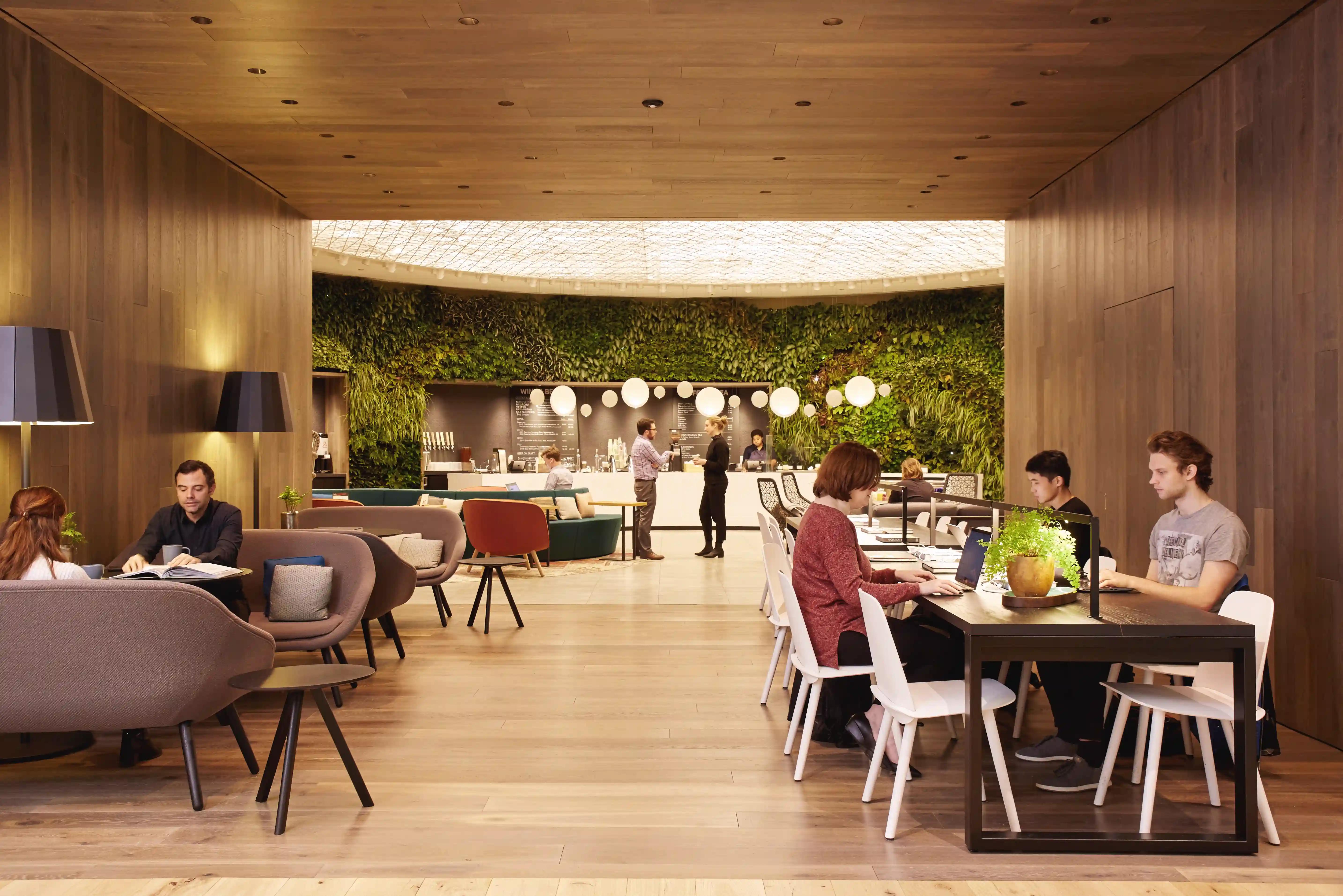 A well lit, earthy looking lounge filled with people enjoying the space. On the far wall is greenery against the bar. Well& by Durst at 151 West 42nd - The Green.