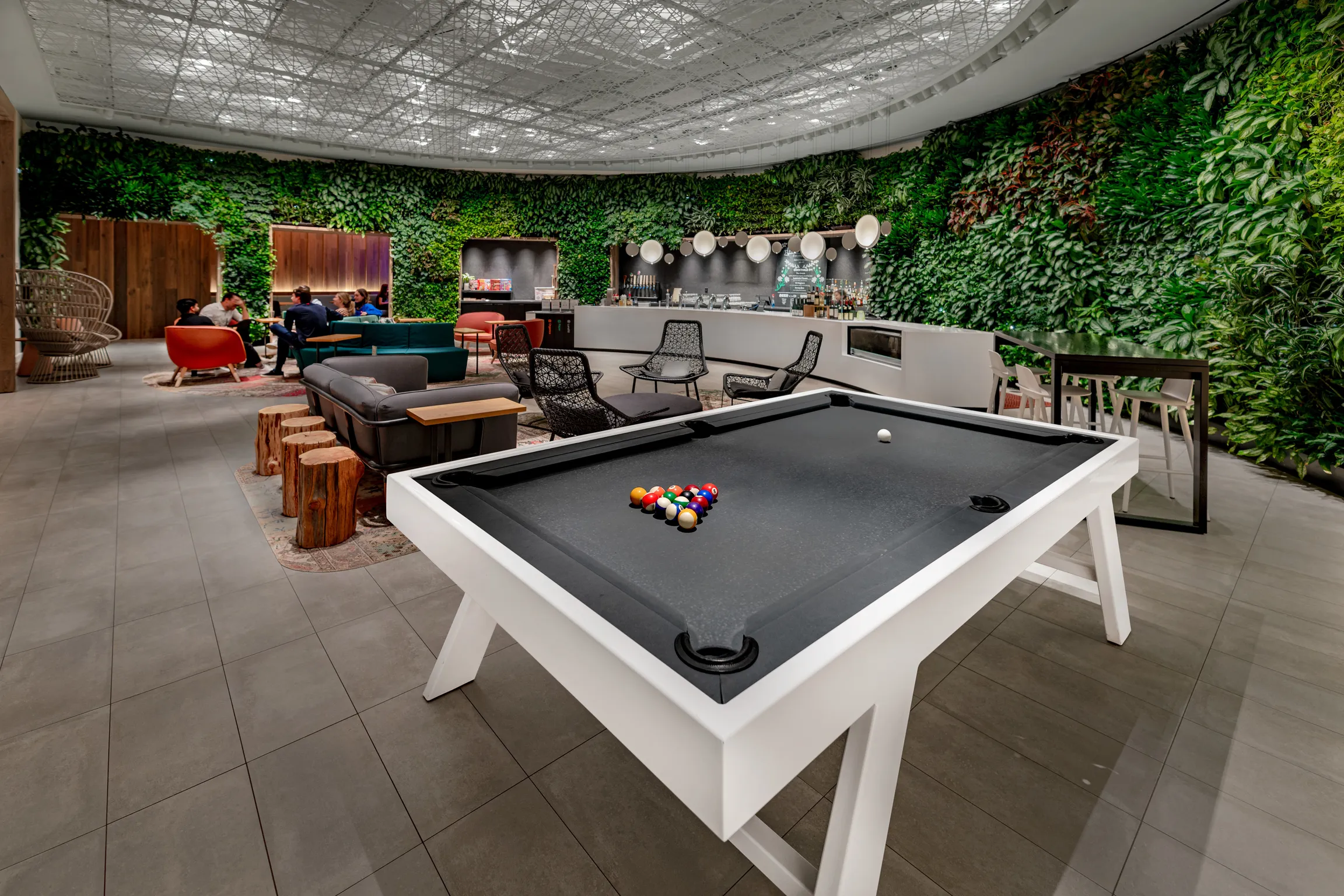 A pool table in a bar lounge with plants on a wall.