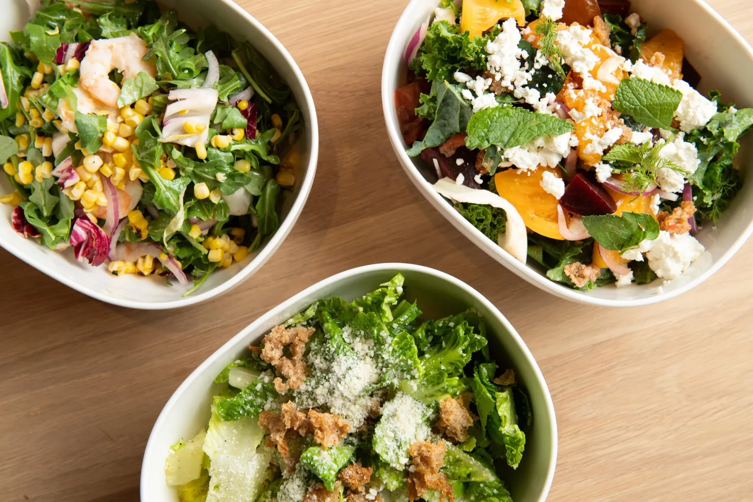 Three bowls of fresh Romaine salad topped with crispy bread crumbs, crumbled feta cheese, and a variety of herbs. Displayed in an appetizing and colorful presentation.