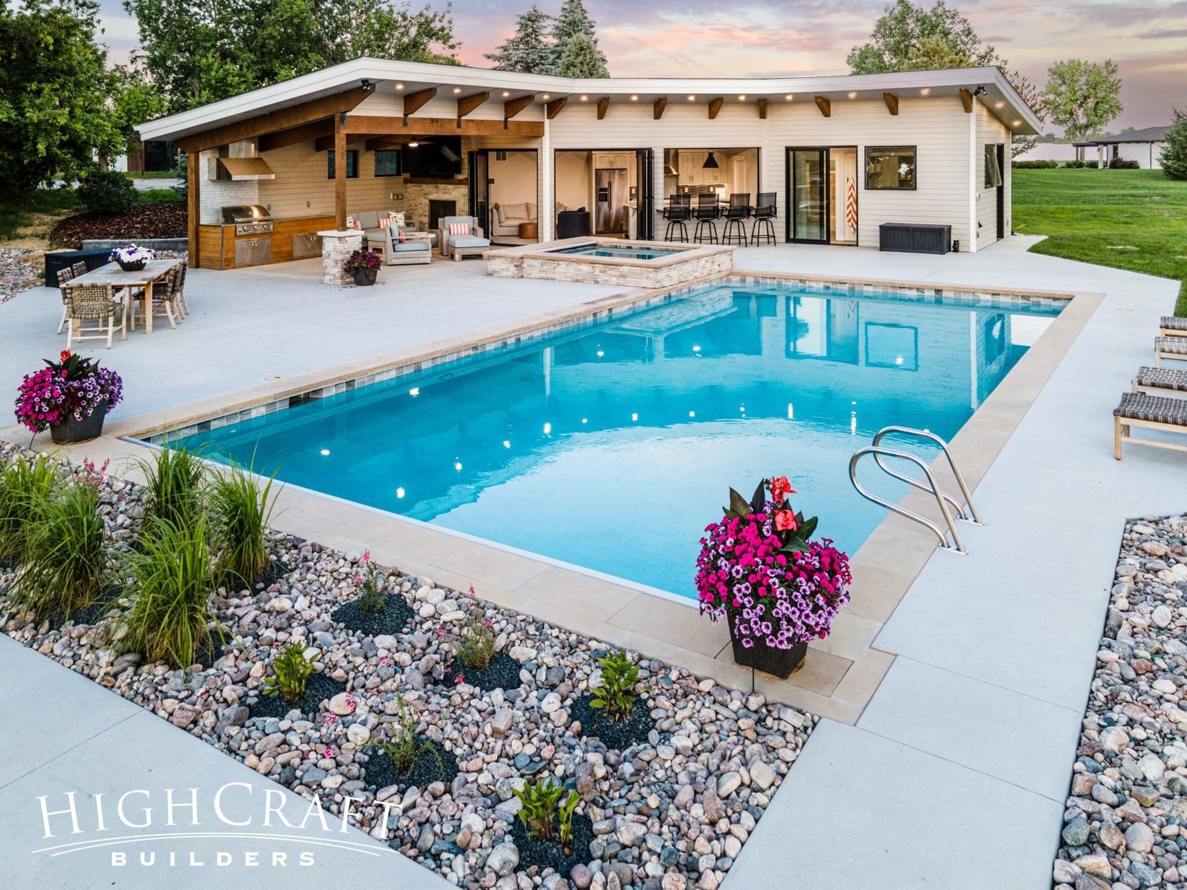 Photo looking at an L-shaped, single-story poolhouse from across the clear, blue pool.  