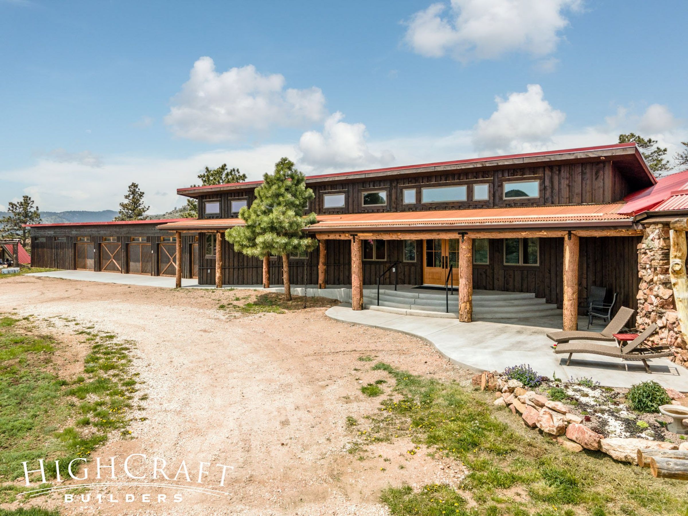 Exterior shot of single-story, woodsy, log-style home with red roof and circular dirt driveway