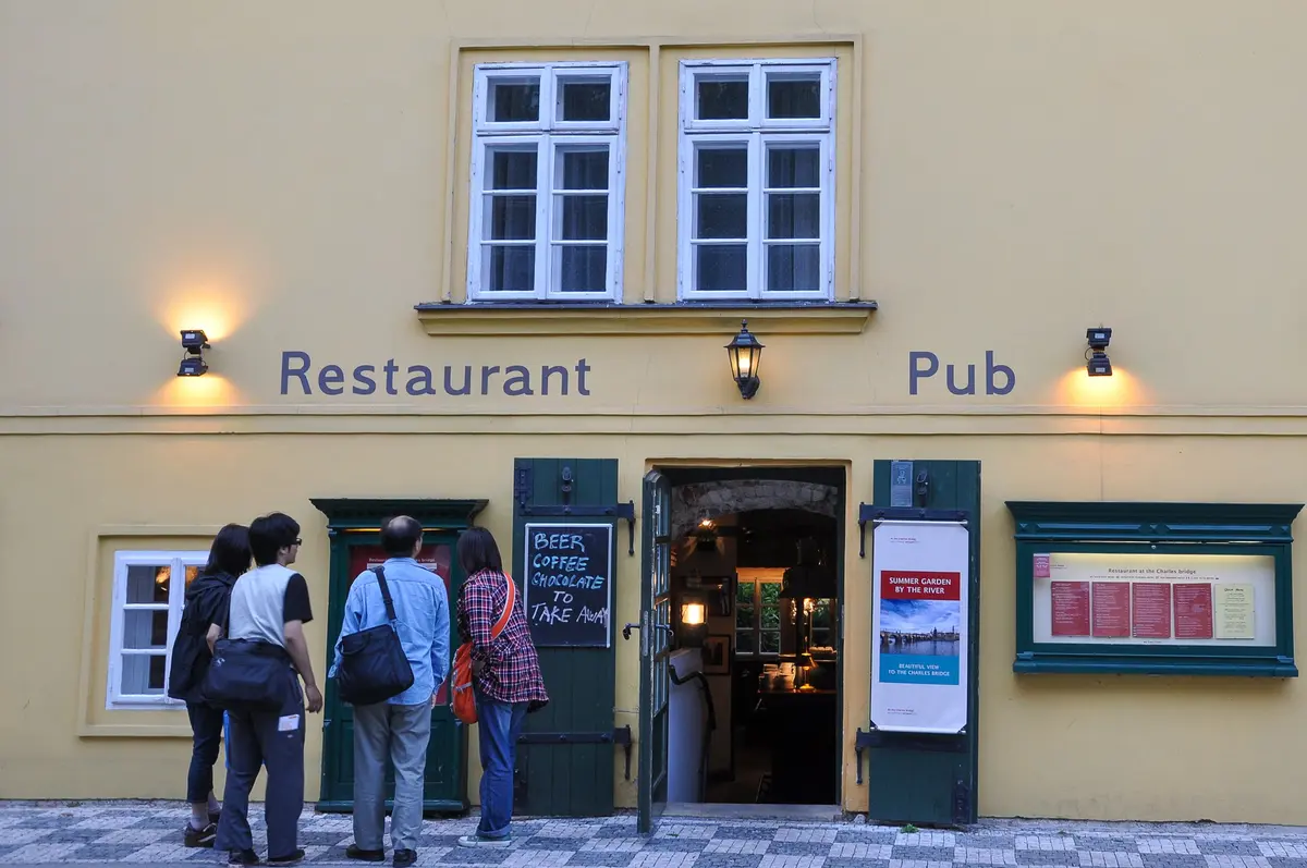 Entrance to a tavern in Prague's historic centre, with travellers reading the menu
