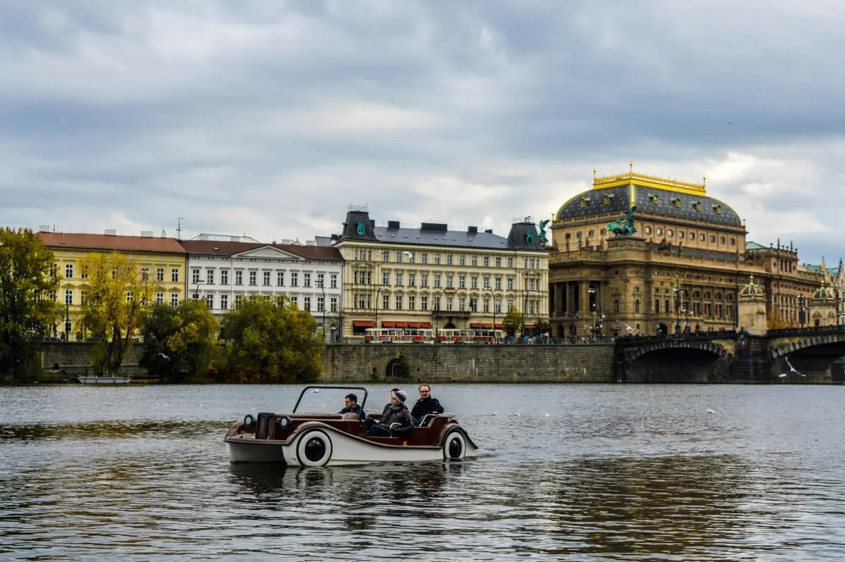 Viajeros navegando el río Moldava cerca del Puente de Carlos en Praga en un dia nublado de abril