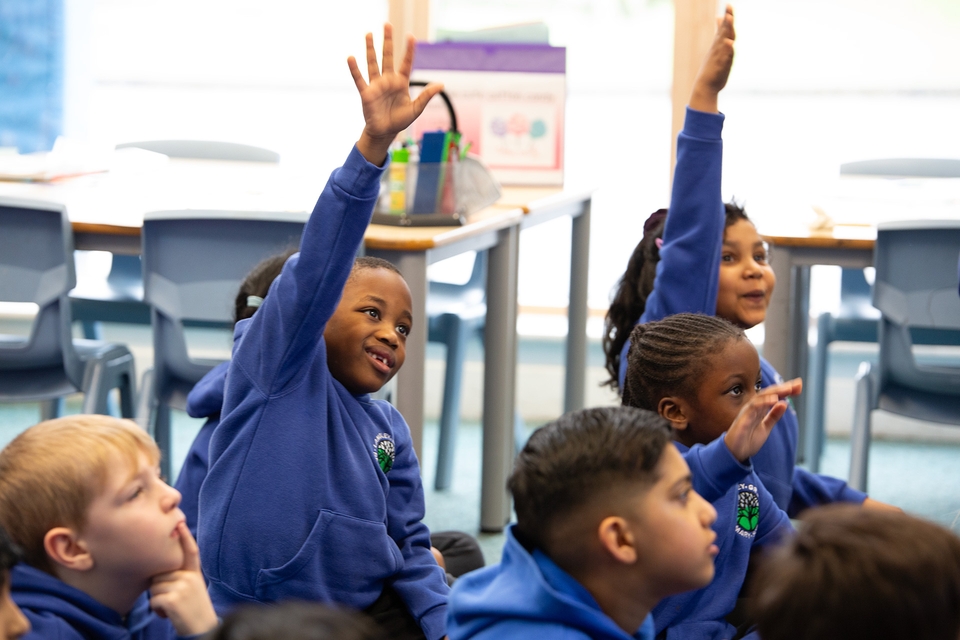 Enthusiastic students in blue uniforms raising hands, engaged in classroom learning