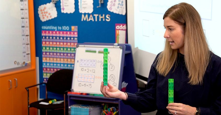 A primary school educator is teaching using green linked cubes inside a classroom