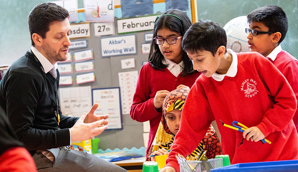 A teacher sits with three pupils explaining a lesson
