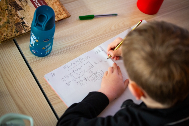 Young male student writing math problem on paper.