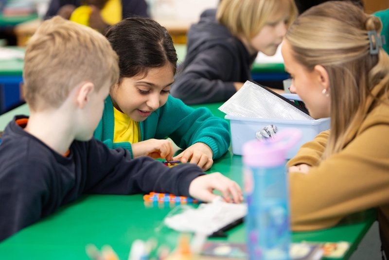 Teacher bent down speaking to students while working with manipulatives.