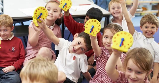 Primary Maths students holding up clocks in the classroom