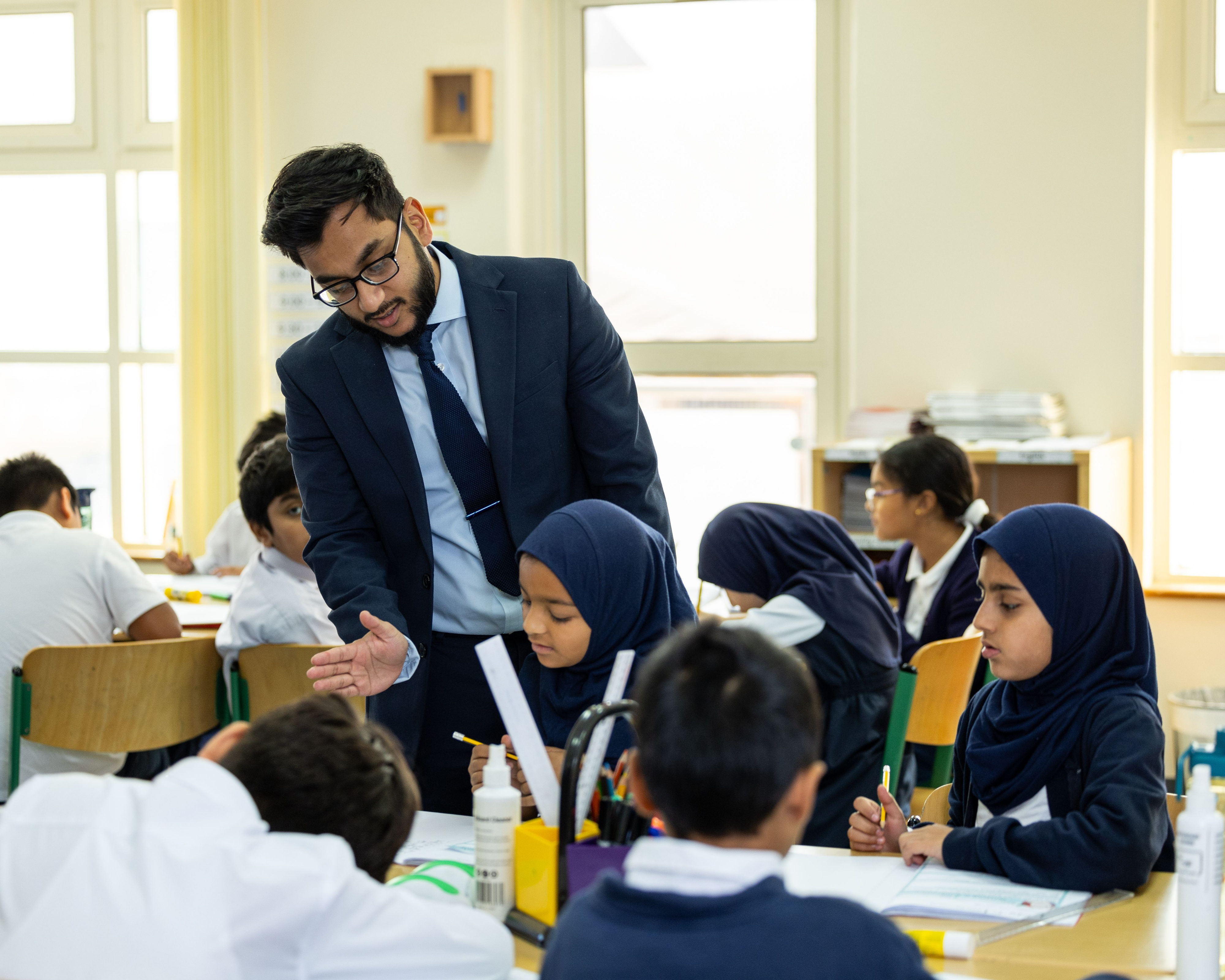 Mesaieed school teacher talking to pupils at their desks with Maths — No Problem! books in front of them.