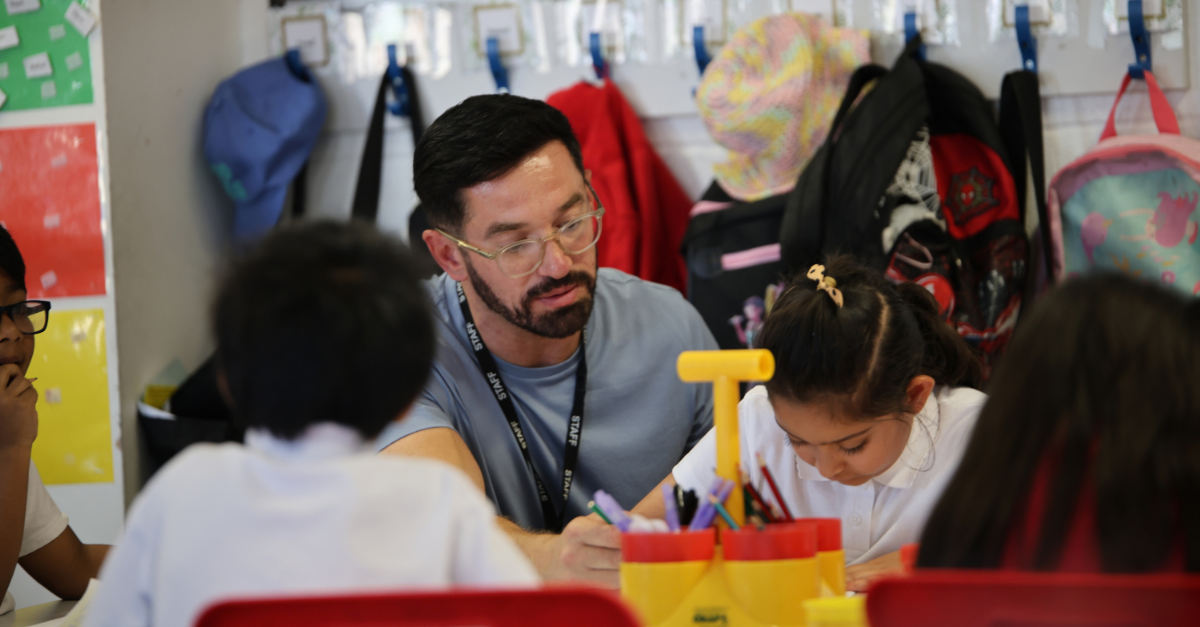 A teacher works with pupils at their desk.