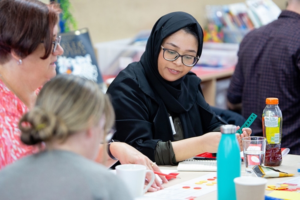 Three female teachers speaking amongst themselves with training materials in front of them.