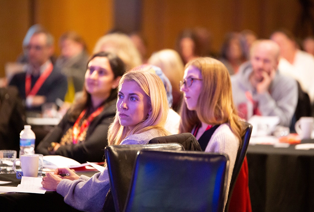 Several CPD conference attendees sitting in round tables with a women in focus in the front row