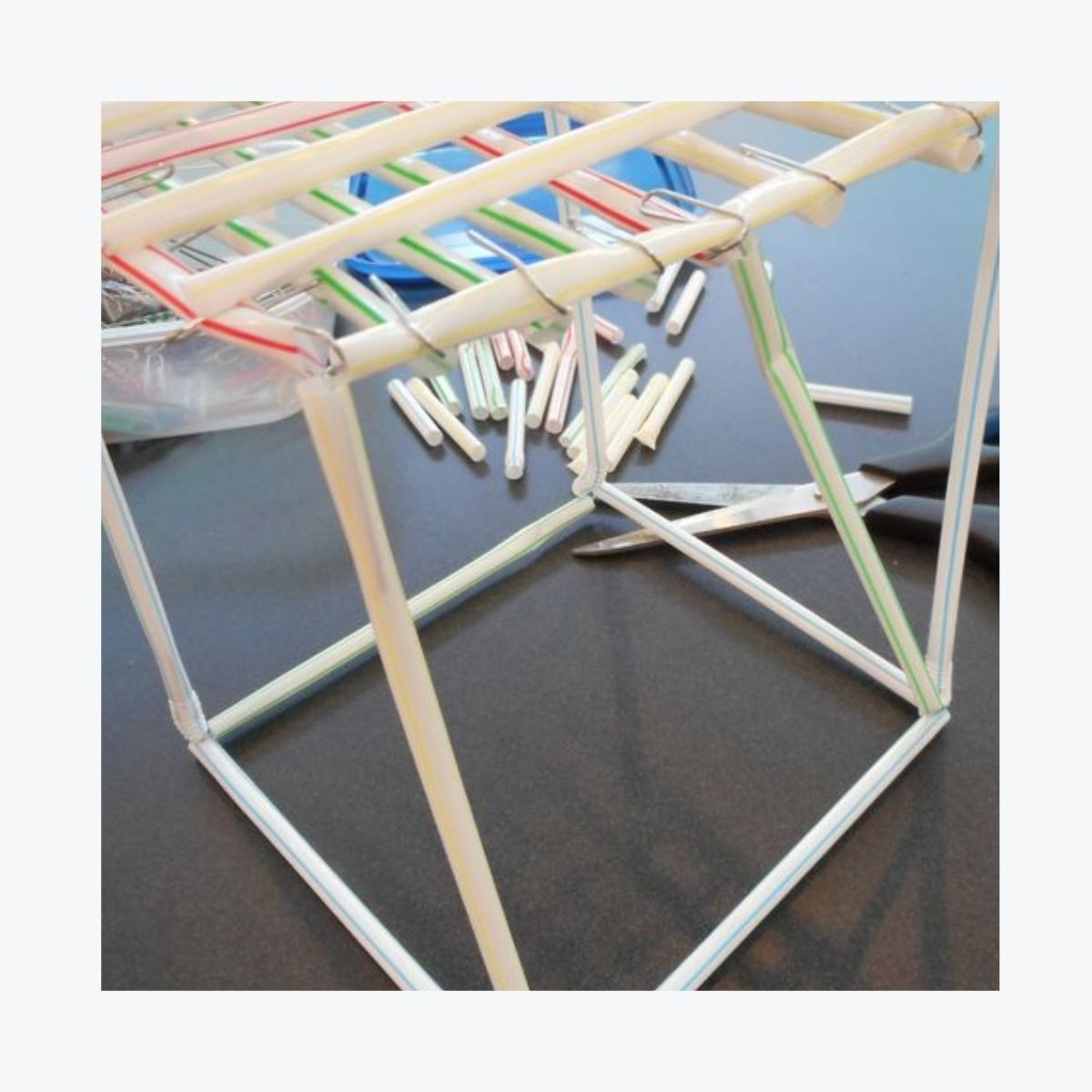 Model structure made from straws, showcasing a simple geometric design with various colourful straws and scissors nearby, ideal for primary school construction projects.