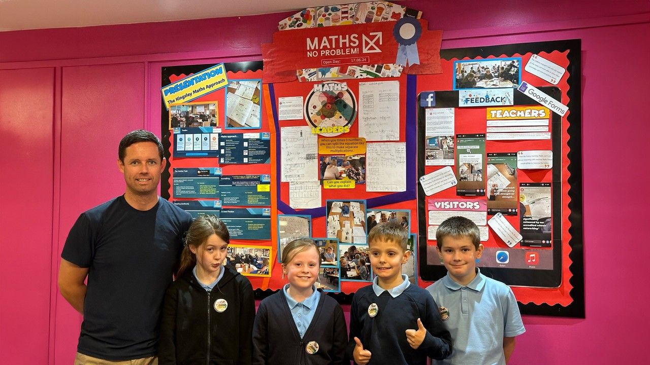 A teacher, Craig Robinson, posing with four young pupils in front of colourful maths-themed bulletin boards