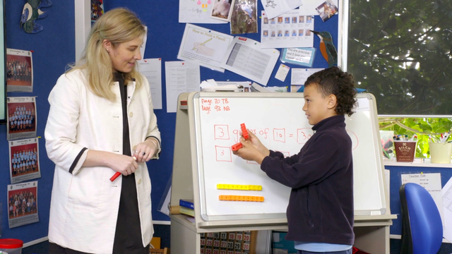 Primary school pupil at front of classroom with teacher