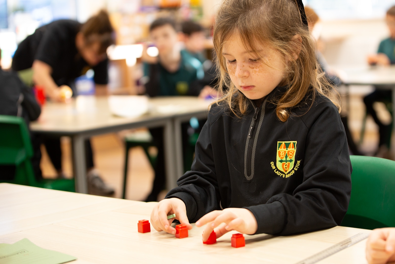 Little girl learning maths with cube manipulatives at a classroom desk.