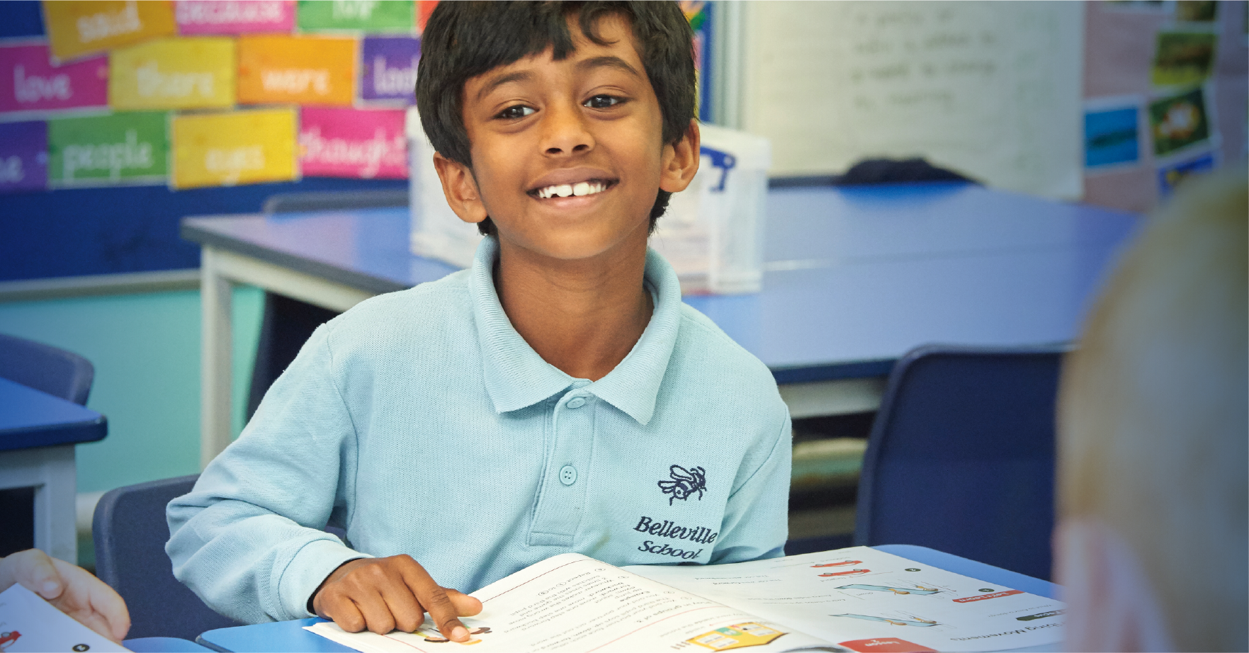A maths mastery student at Belleville Primary looking up from maths textbook and smiling.