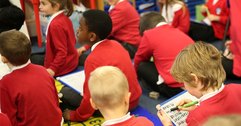 Rows of maths pupils in classroom with personal whiteboards.