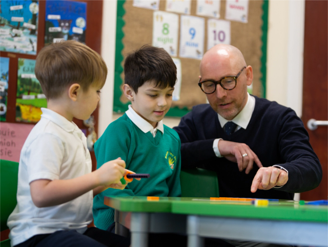 Teacher talking to two pupils with manipulatives.