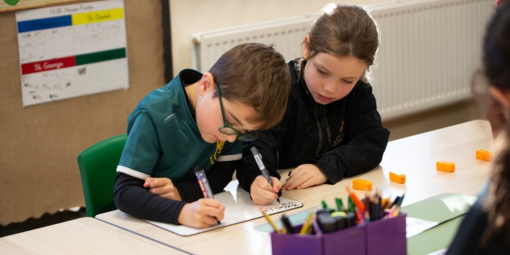 Two young pupils writing on a mini whiteboard together.