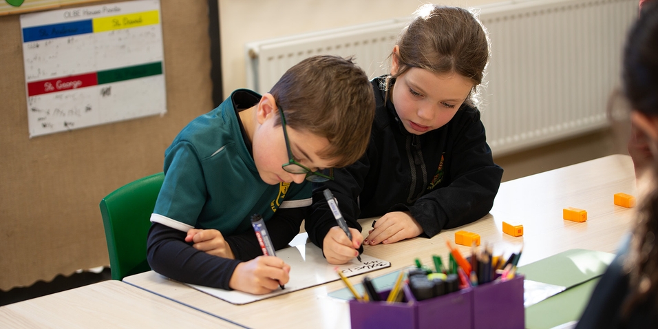 Two young pupils writing on a mini whiteboard together.